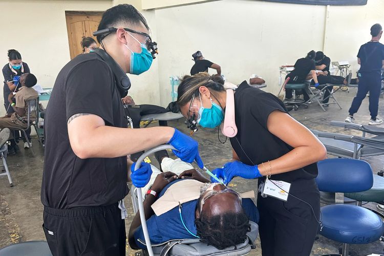 two student dentists giving dental care to a patient in a dental chair